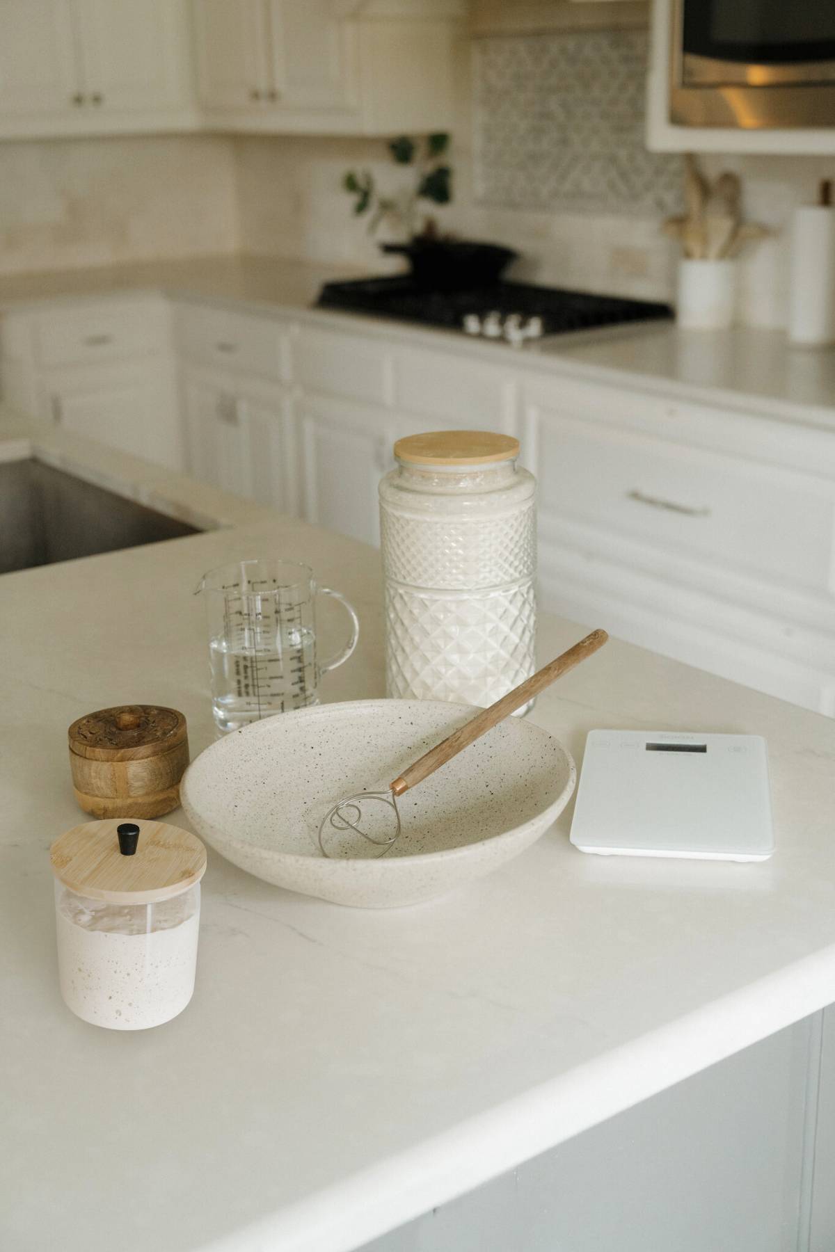 on the counter of a kitchen rest the ingredients to make sourdough bread. Water, flour, salt, and sourdough starter