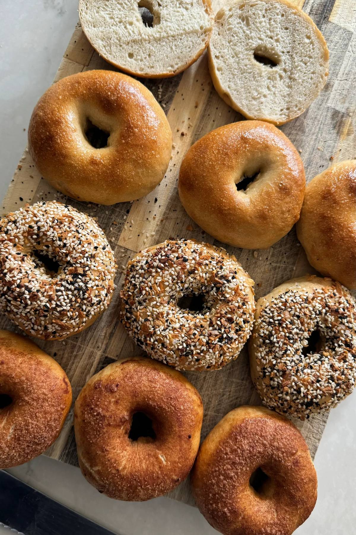 sourdough bagels, some are plain, some are topped with everything bagel seasoning, or cinnamon sugar, and one is sliced in half