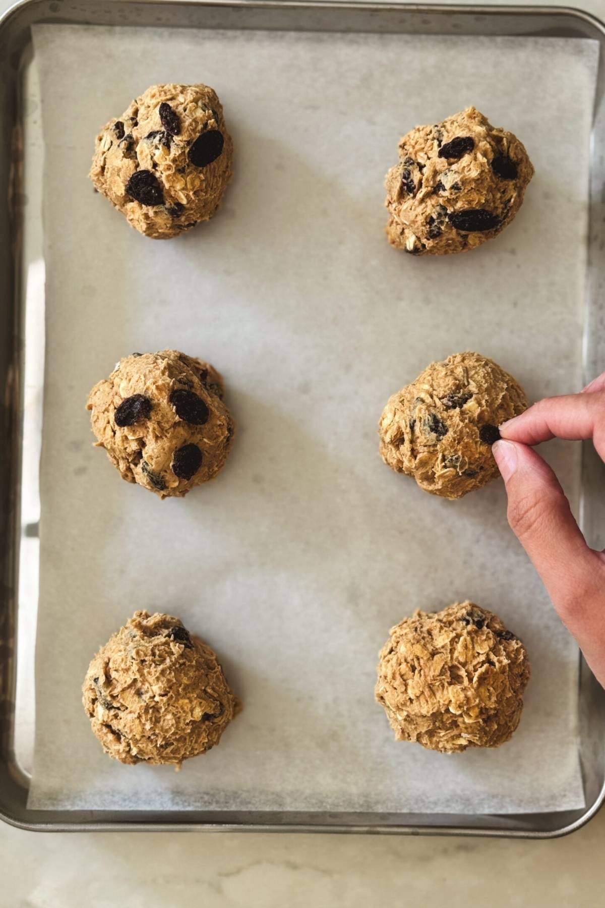 putting more raisins on top of the oatmeal raisin cookie dough balls before baking