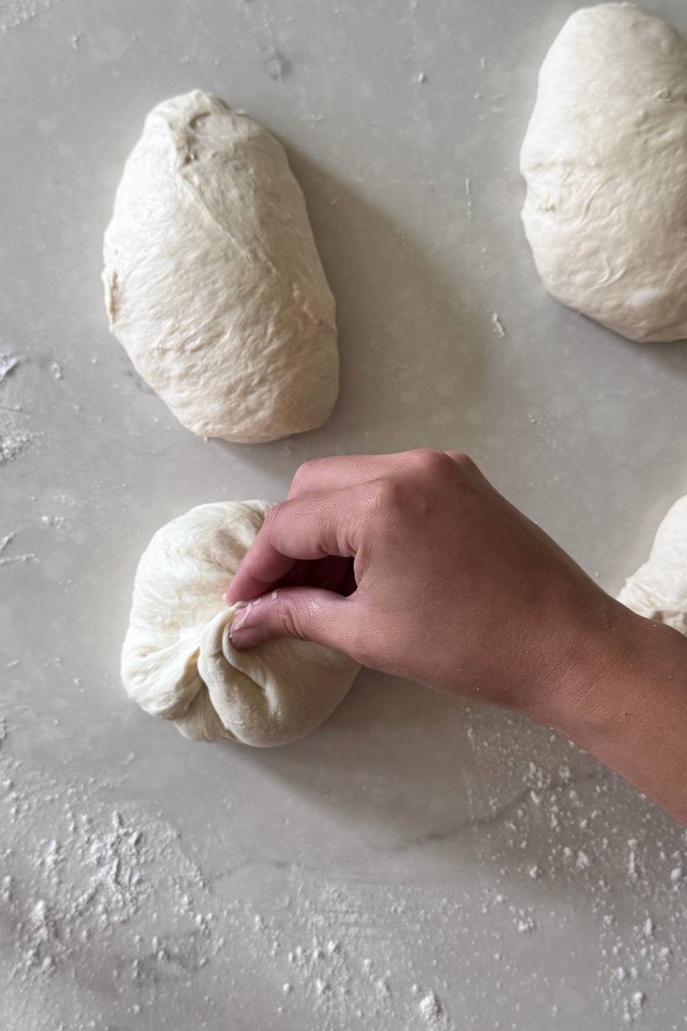 shaping sourdough pizza dough into balls by pinching all sides in the middle