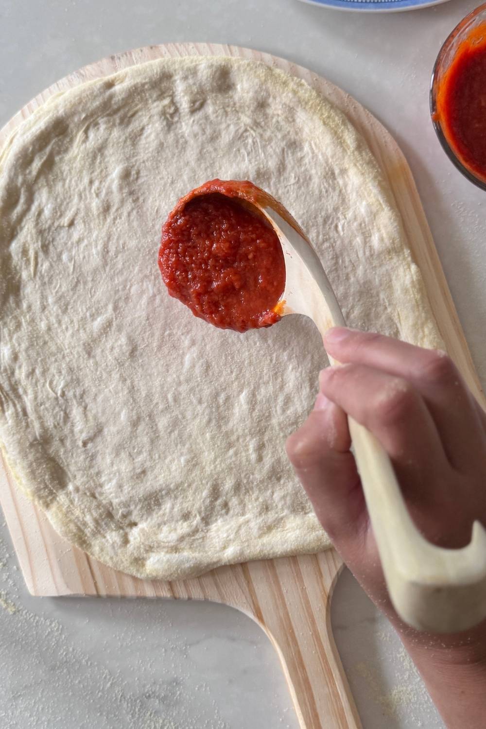 spreading sauce over sourdough pizza dough 